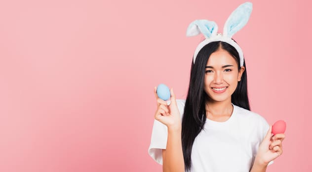 Happy Easter concept. Beautiful young woman smiling wearing rabbit ears holding colorful Easter eggs gift on hands, Portrait female looking at camera, studio shot isolated on pink background