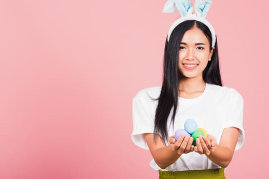 Happy Easter concept. Beautiful young woman smiling wearing rabbit ears holding colorful Easter eggs gift on hands, Portrait female looking at camera, studio shot isolated on pink background