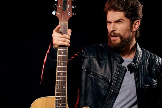 A man with a guitar in his hands leather jacket music performance rock star modern style dark background. High quality photo
