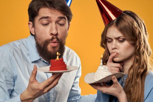 Birthday party man and woman on a yellow background in hats with a cake in their hands. High quality photo