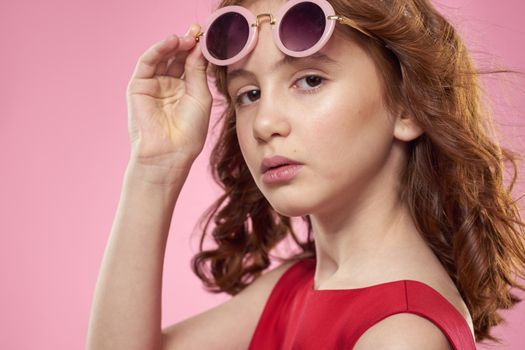 Girl with curly hair dark round glasses fun red dress pink background. High quality photo