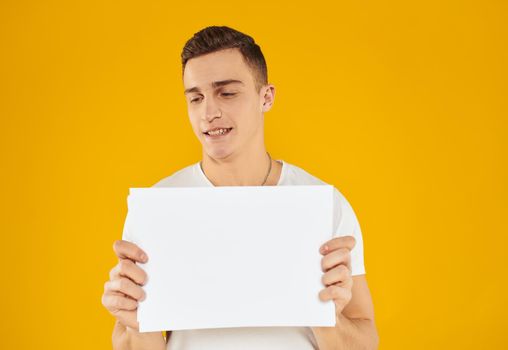 A man in a white T-shirt with a sheet of paper on a yellow background Copy Space mockup. High quality photo