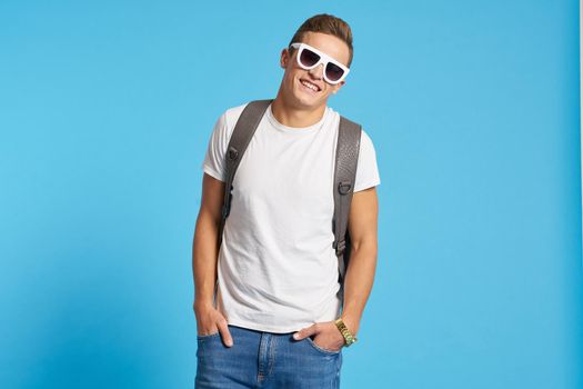 Relaxed guy in jeans with torn knees sits on a chair indoors on a blue background with full-length glasses on his face. High quality photo