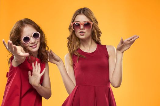 cheerful mom and daughter wearing sunglasses lifestyle friendship family yellow background studio. High quality photo