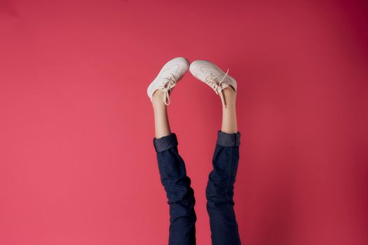 Inverted female legs white sneakers motion street style pink background. High quality photo