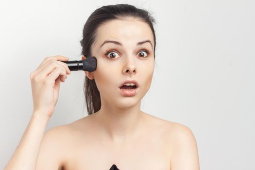 woman with bare shoulders applying makeup brush on face. High quality photo