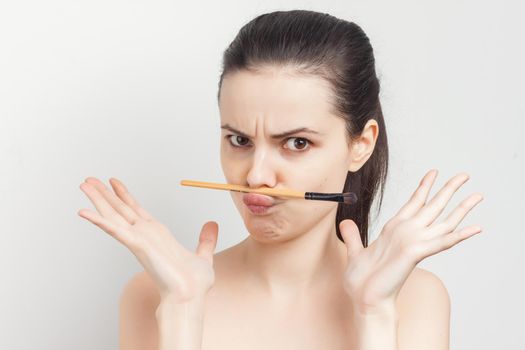 brunette holding makeup brush skin care face cream bare shoulders. High quality photo