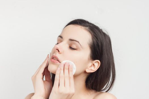 brunette naked shoulders wipes her face but clean skin with a sponge. High quality photo