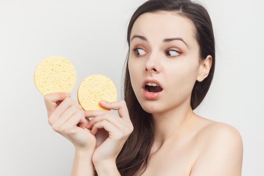 brunette naked shoulders wipes her face but clean skin with a sponge. High quality photo