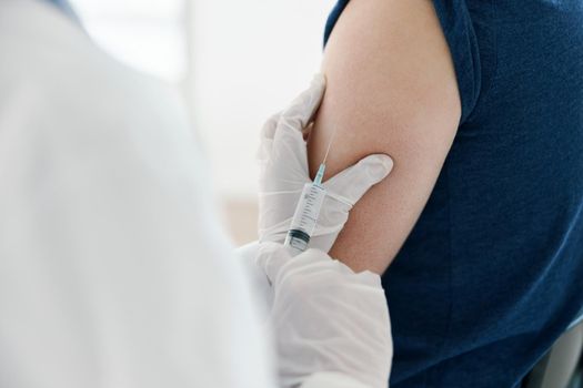 woman doctor in a medical mask injecting a man in a blue t-shirt. High quality photo