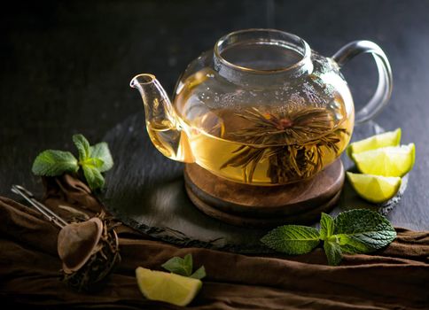 Teapot with tea surrounded with green leaves, tea ceremony, green tea in a transparent cup