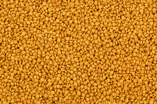 full frame background an seamless texture of small dry orange cat food crockets.
