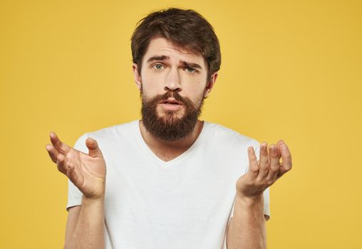 Emotional brunette man gestures with his hands on a yellow background. High quality photo