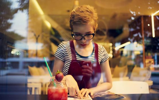 fashionable woman in red sundress sits in a cafe and mirror glass reflection of cars on the street. High quality photo