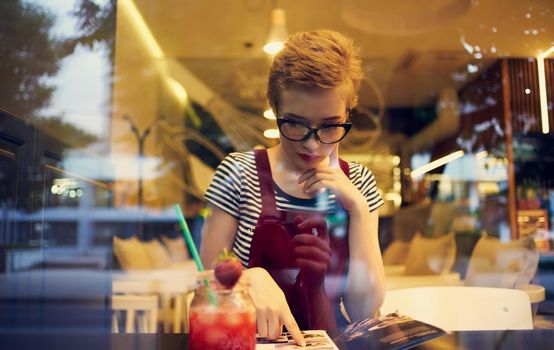 women in a sundress sitting in a cafe and looking at the street through the glass. High quality photo