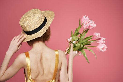 woman with hat back view bouquet of flowers as a gift pink background. High quality photo