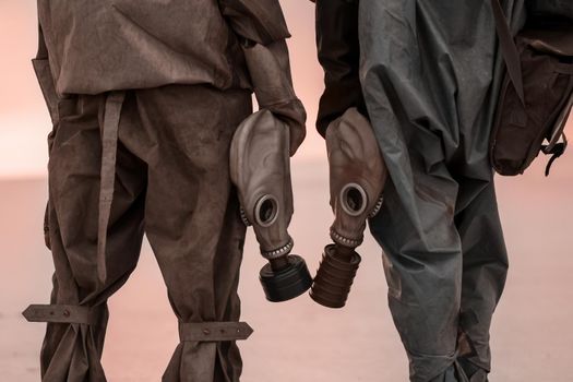 Two people with gas masks and chemical protection suits on the background of the scorched dead earth. post. Apocalypse. Survivors of a nuclear war.