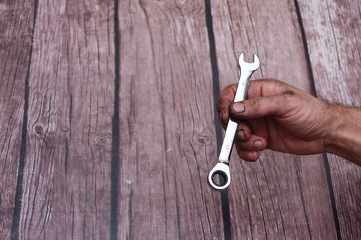 Male hand worker holding wrench, on a wooden background. With an inscription. International celebration. Labor Day. empty space