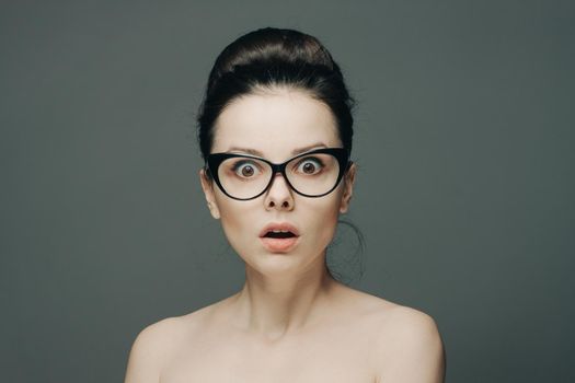 surprised woman with glasses naked shoulders gathered hair gray background. High quality photo