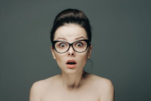 woman with glasses naked shoulders gathered hair gray background. High quality photo