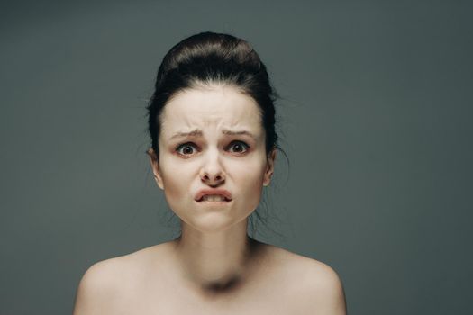 frightened woman's face naked shoulders hairstyle gray background model. High quality photo