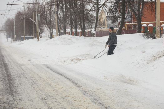 Tula, Russia - February 13, 2020: Man cleaning driveway from snow with scraper at winter morning after snowstorm, close-up with selective focus.