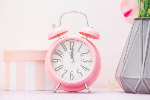 Gentle pink alarm clock next to a vase of flowers and a decorative gift box in a scandinavian style kitchen
