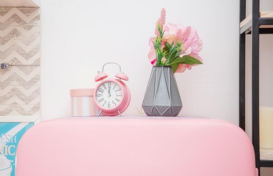 A vase of flowers and a pink alarm clock on the roof of a pink refrigerator in a bright Scandinavian style kitchen