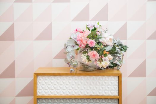A vase of flowers on a chest of drawers near the wall with a geometric pattern in a light pink living room