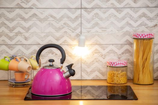A kettle on a two-burner stove in a bright pink Scandinavian-style kitchen.
