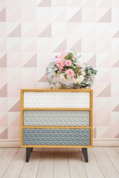 A vase of flowers on a chest of drawers near the wall with a geometric pattern in a light pink living room