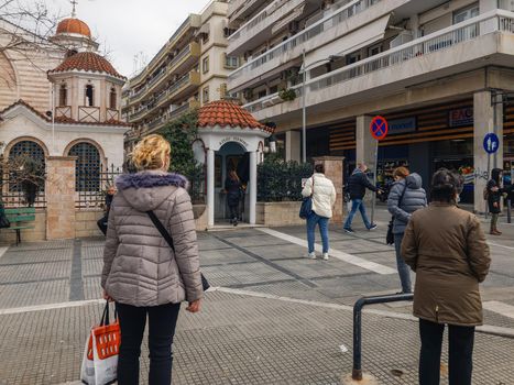 Greeks with coronavirus masks wait to practice their religious worship outside an Orthodox church.