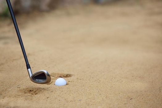 Golf ball and club in sand bunker at golf course