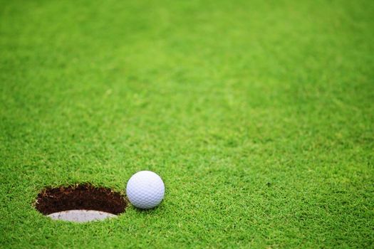 Golf ball close to hole, on lip of cup on green of golf course background with copy space for text banner