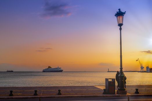 Evening view of commercial boat entering calm sea harbor, with Hellenic flag waiving on a crane