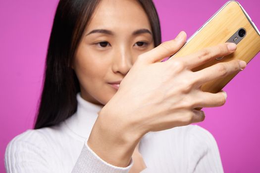 woman asian appearance phone in hands close-up technology gadget pink background. High quality photo