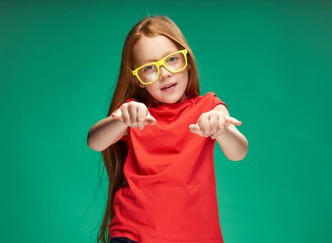 cute red-haired girl gesturing with her hands childhood green background school. High quality photo