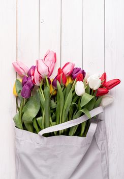 Eco friendly, zero waste concept. Gray fabric bag full of colorful tulips on white wooden background