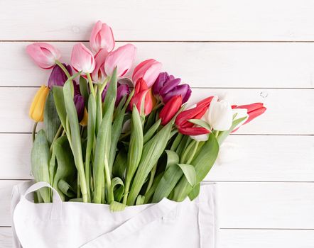 Eco friendly, zero waste concept. Gray fabric bag full of colorful tulips on white wooden background