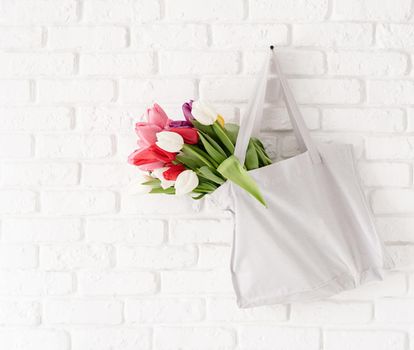 Eco friendly, zero waste concept. Gray fabric bag full of colorful tulips on white brick background