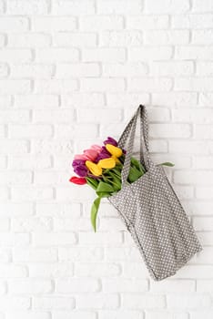 Eco friendly, zero waste concept. Gray polka dot fabric bag full of colorful tulips on white brick background