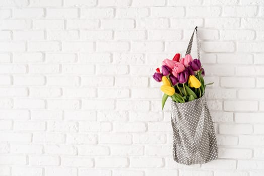 Eco friendly, zero waste concept. Gray fabric bag ful of colorful tulips on white brick background