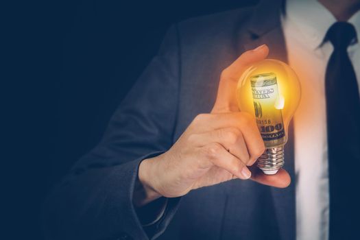 Hand of businessman holding light bulb having currency dollar, success of finance, innovation and energy, planning with financial saving, vision and knowledge, lightbulb glowing, business concept.