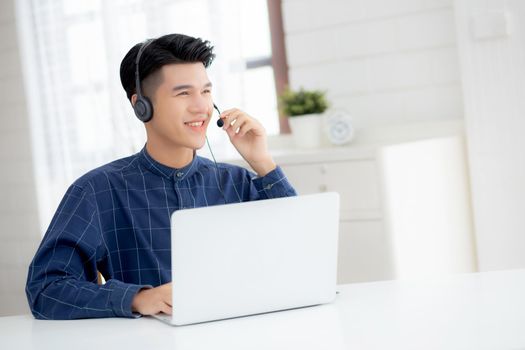 Young asian businessman working on laptop computer wearing headphone at home, business man wearing headset for video conference, communication and education, male study and learning for e-learning.