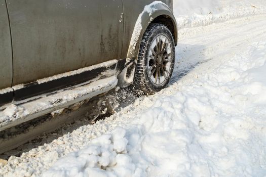 Road snow flies up from a dirty vehicle's spinning wheel. Car's wheels spin and spew up pieces of snow it attempts to gain traction on the slippery road at winter daytime.