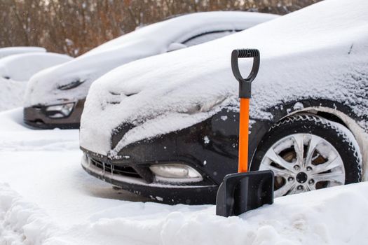 plastic snow shovel in front of snow-covered car at sunny winter morning, close-up with selective focus