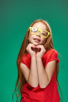 cute red-haired girl with glasses gesturing with her hands school childhood green background. High quality photo