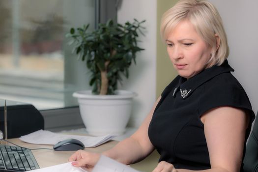 A female director working in an office is sitting at a table, analyzing business statistics, checking documents. Close-up.