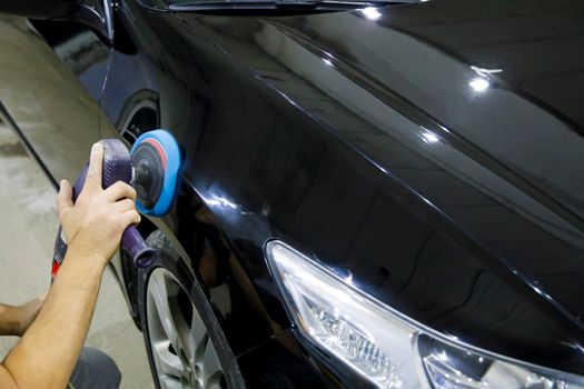 Male hands polish the car with a soft disk machine. Selective focus