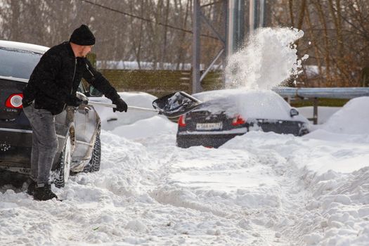 Tula, Russia - February 13, 2020: Man digs snow from under the car at winter day.